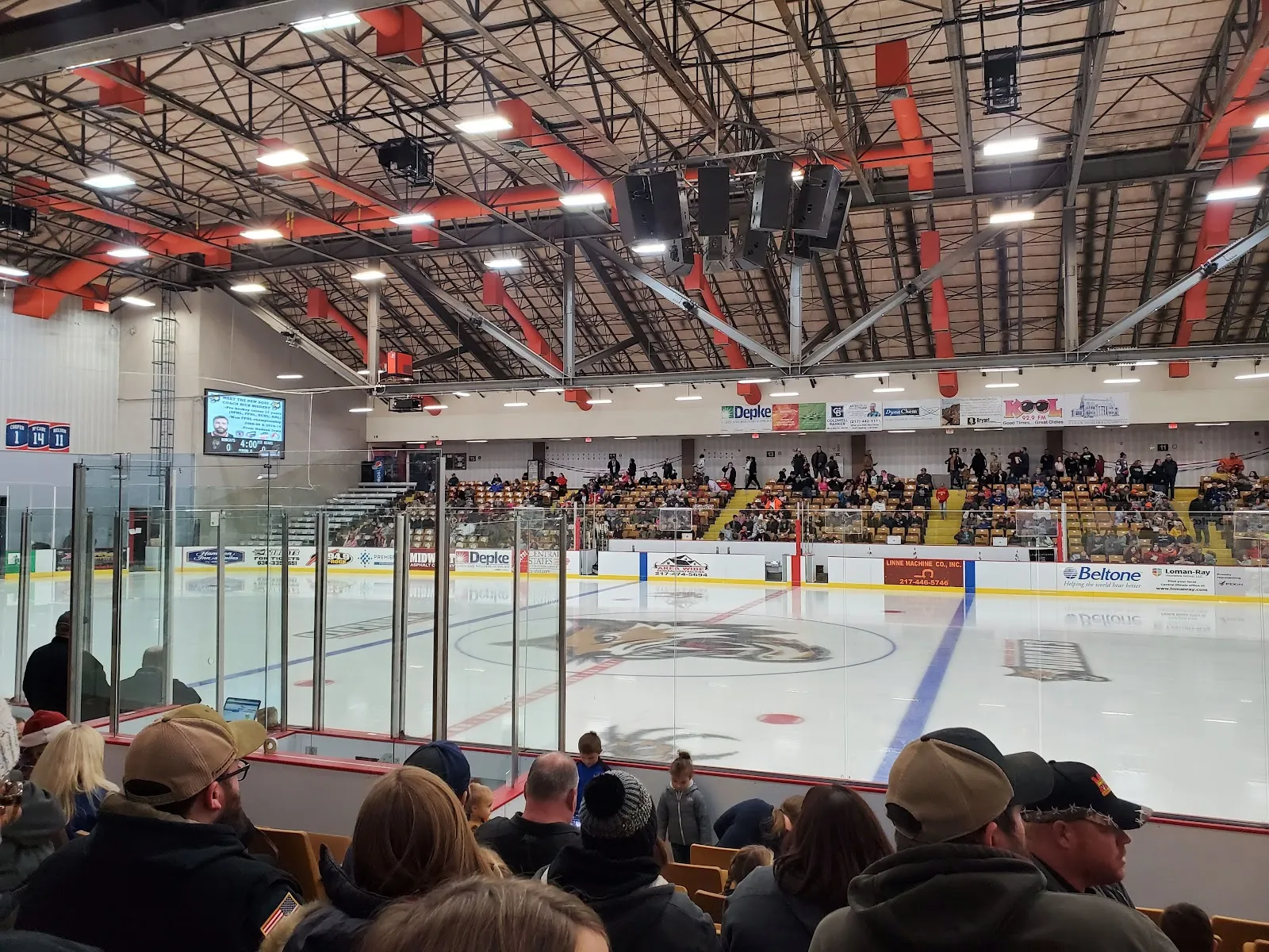 A hockey game on the ice at David S. Palmer Arena seen from the seats, with the spectator stands beyond the boards — David S. Palmer Arena