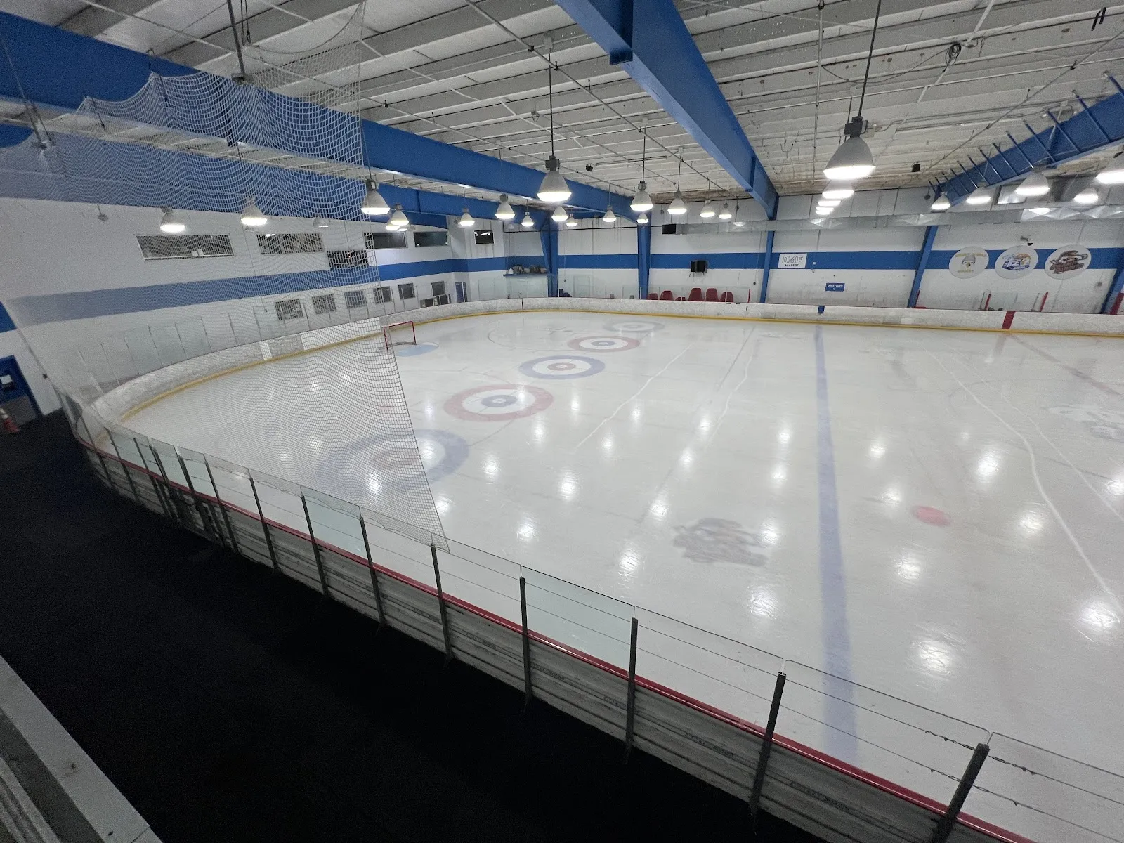 La pista vacía de tamaño NHL con los anillos de la casa de curling, bajo las vigas azules de acero del techo. — Daytona Ice Arena
