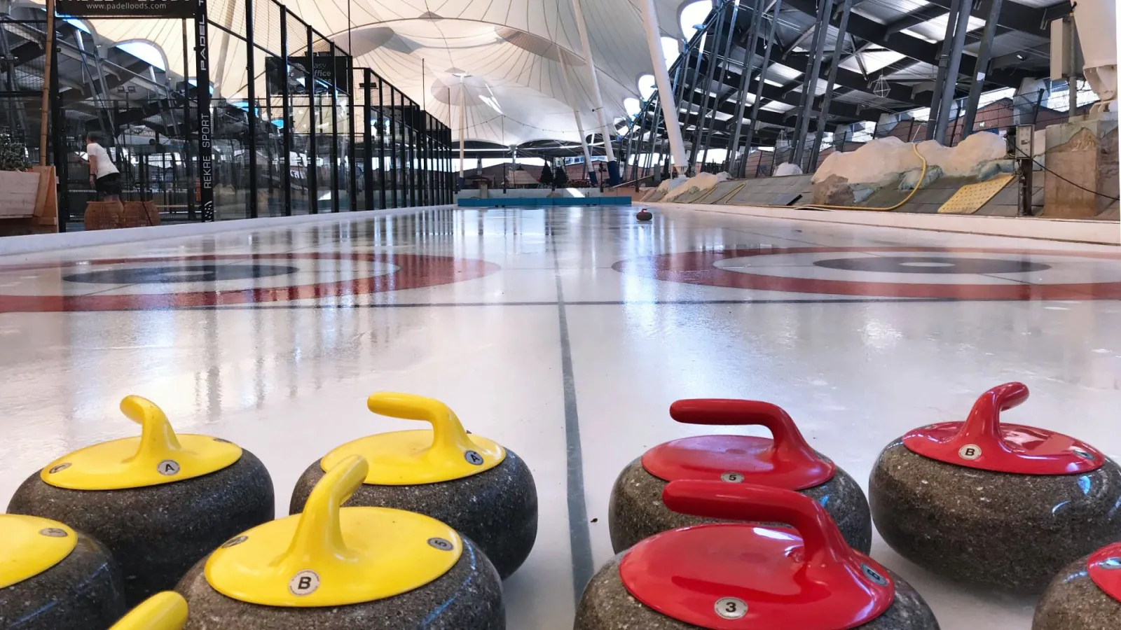 The curling lane and granite stones on the ice at De Scheg, under the tent roof — De Scheg ijsbaan