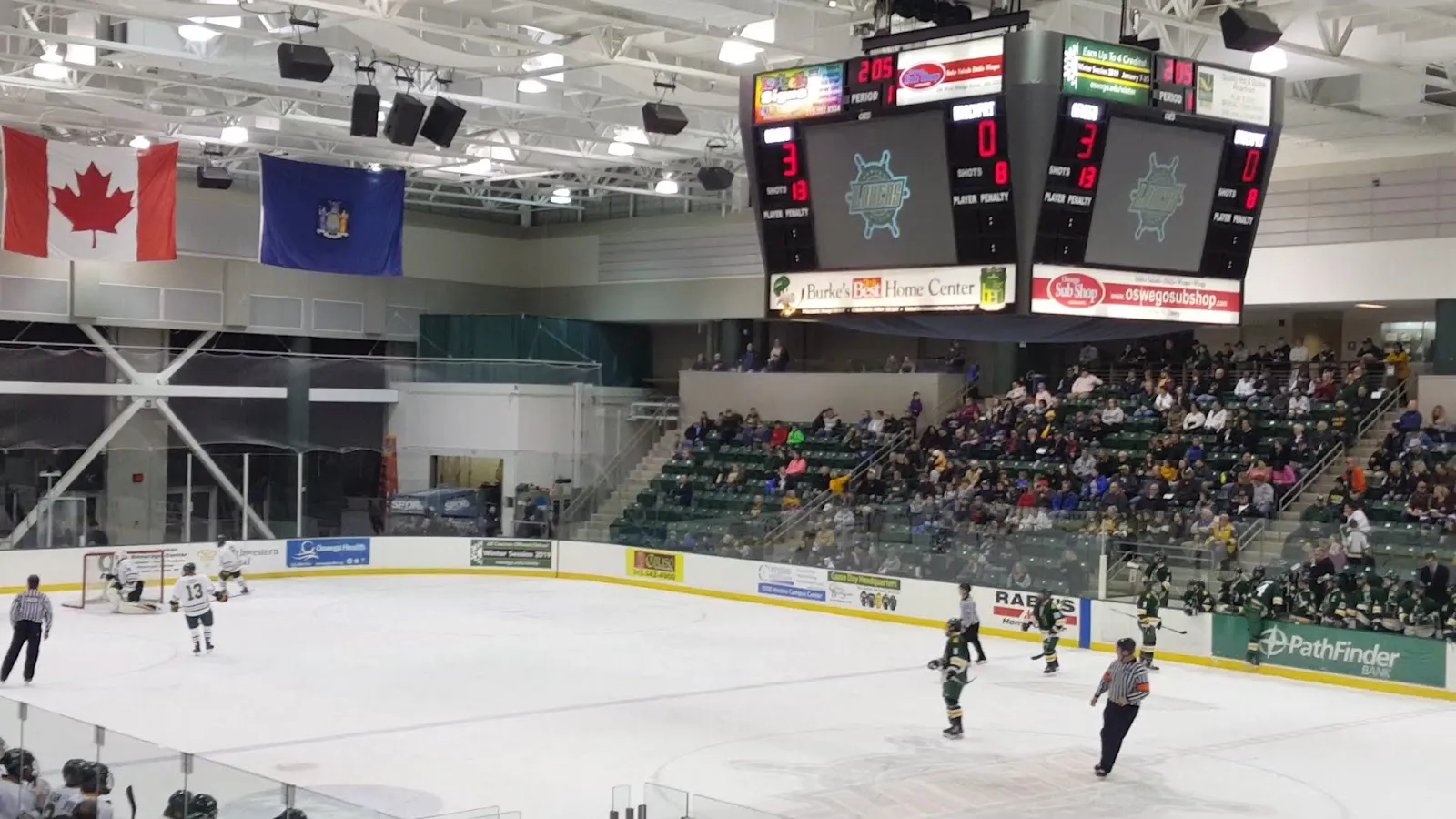 An Oswego State hockey game in the Deborah F. Stanley Arena, with the scoreboards, flags and the stands behind the boards — Deborah F. Stanley Arena (SUNY Oswego)