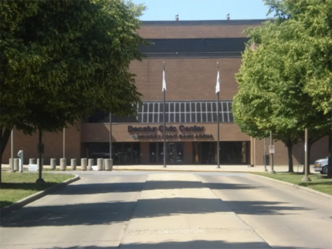Front entrance of the Decatur Civic Center, a brick building with 'Decatur Civic Center' and 'Hickory Point Bank Arena' signage above glass doors, flanked by trees and flagpoles. — Decatur Civic Center