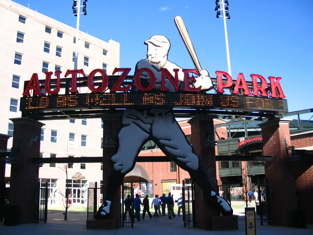The AutoZone Park entrance gate in Memphis, with the neon batter sign over the arch and people walking in. — Deck the Diamond at AutoZone Park