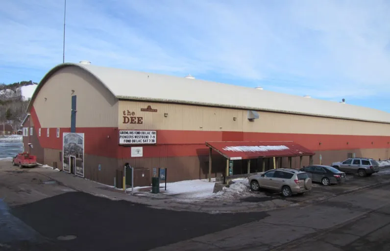 The Dee on the Houghton waterfront, with the rink building's curved roof and the Dee sign over the entrance. — Dee Stadium