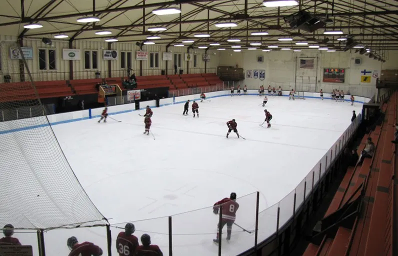 A hockey game on the ice at Dee Stadium, with the red grandstand along the boards. — Dee Stadium