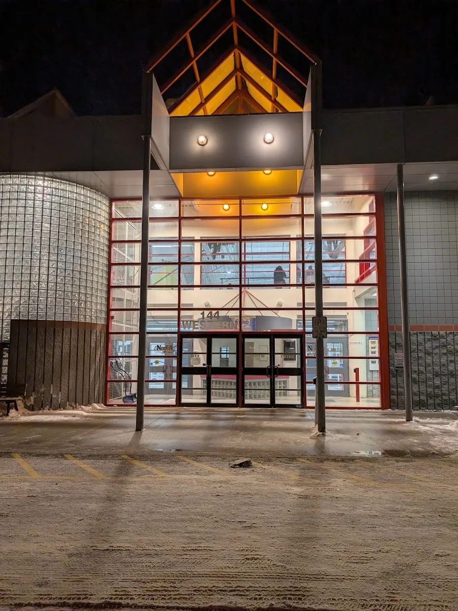 The Delhi arena entrance at night: a tall glass entry with a lit peaked canopy and "144 Western" on the glass. — Delhi Arena