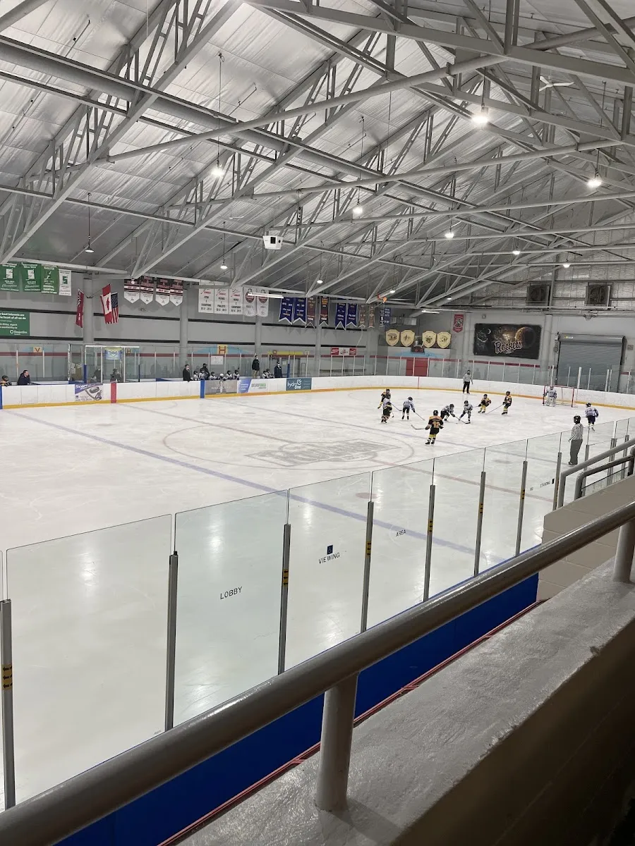 The Delhi arena ice from the rail above the glass during a hockey practice, with banners along the far wall under a white steel roof. — Delhi Arena