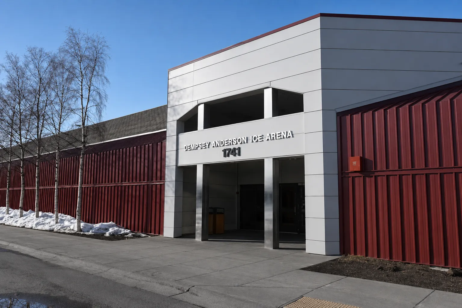 The Dempsey Anderson Ice Arena entrance, a white block with the arena name and 1741 above the doors between red metal walls. — Dempsey Anderson Ice Arena