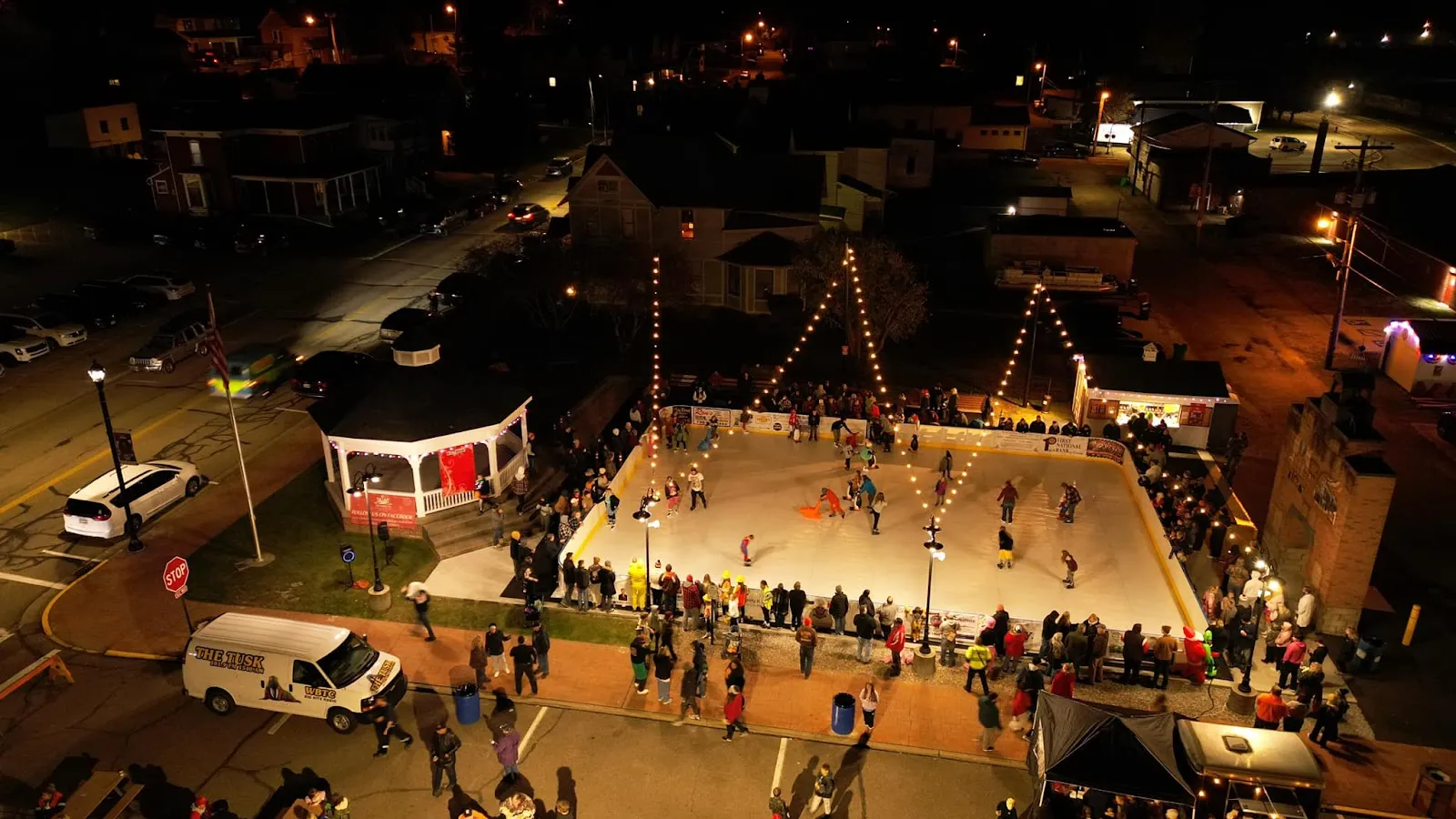 Aerial view at night of the Dennison ice rink in the town square, with spectators and skaters at a distance — Dennison Ice Skating Rink