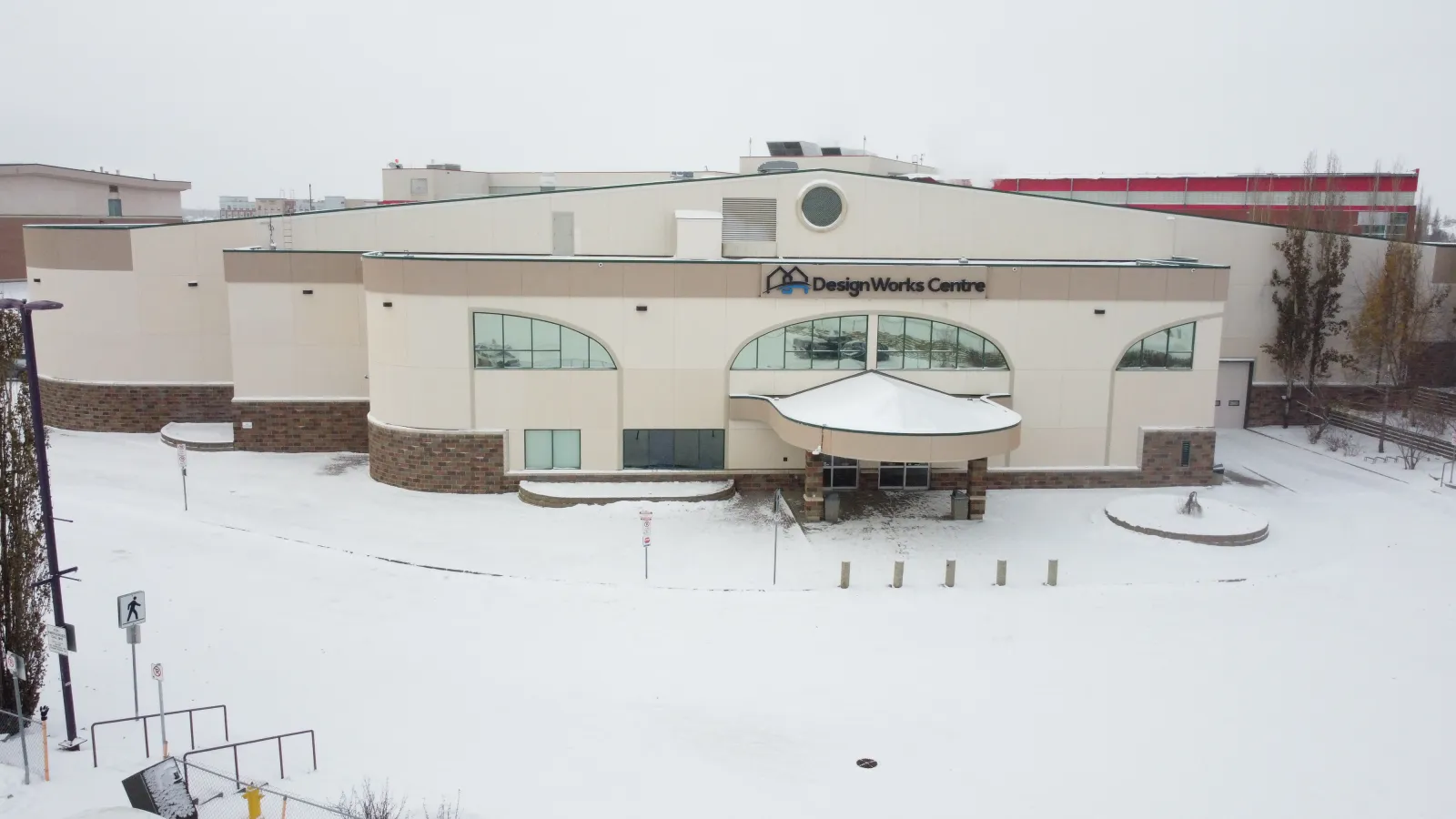 The Design Works Centre from the air in early snow, its arched windows and entrance canopy under the DesignWorks Centre sign. — Design Works Centre