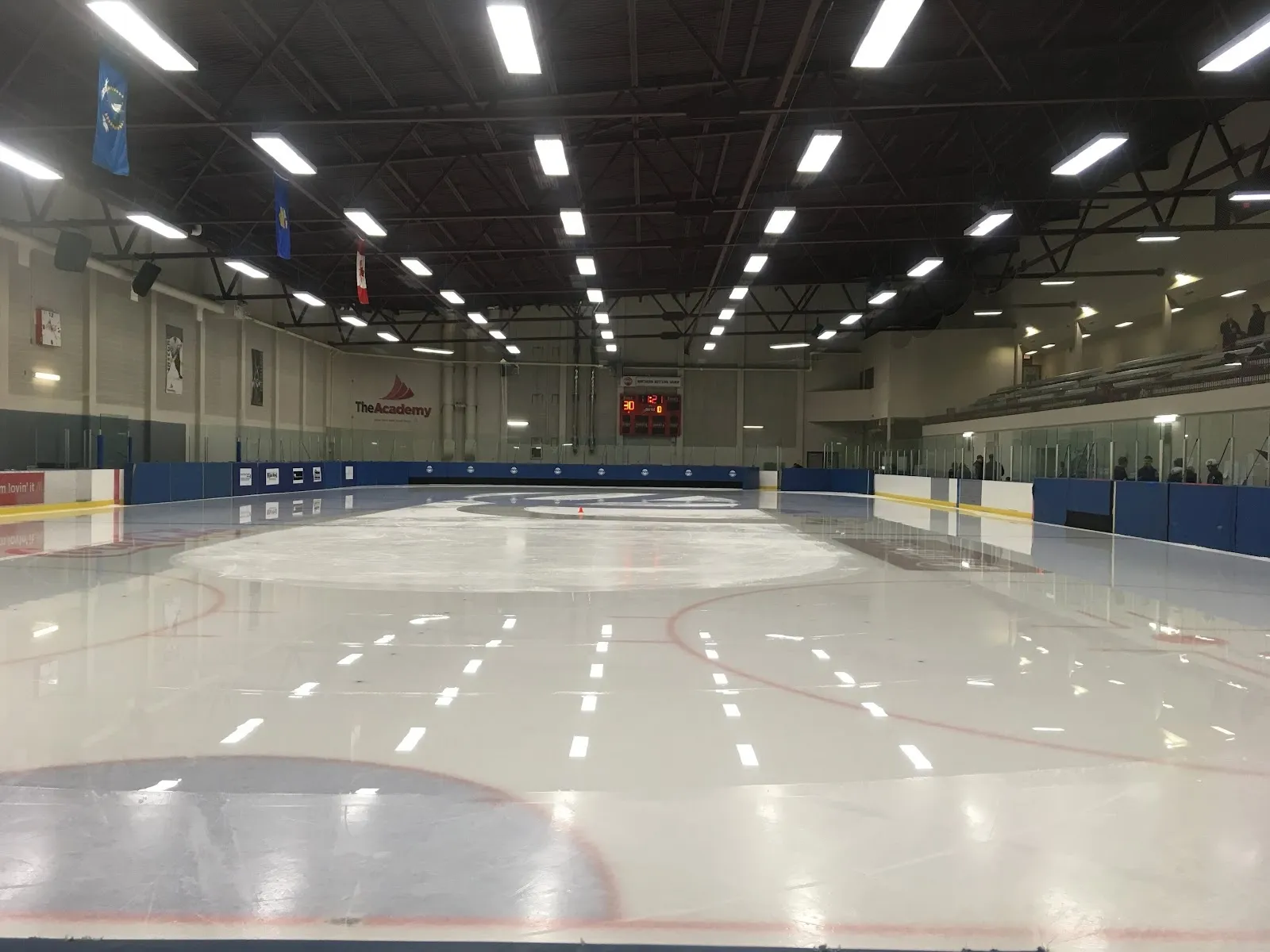 A wide empty sheet with blue and white markings seen from the end, a bright ceiling of lights above rows of long fixtures. — Design Works Centre