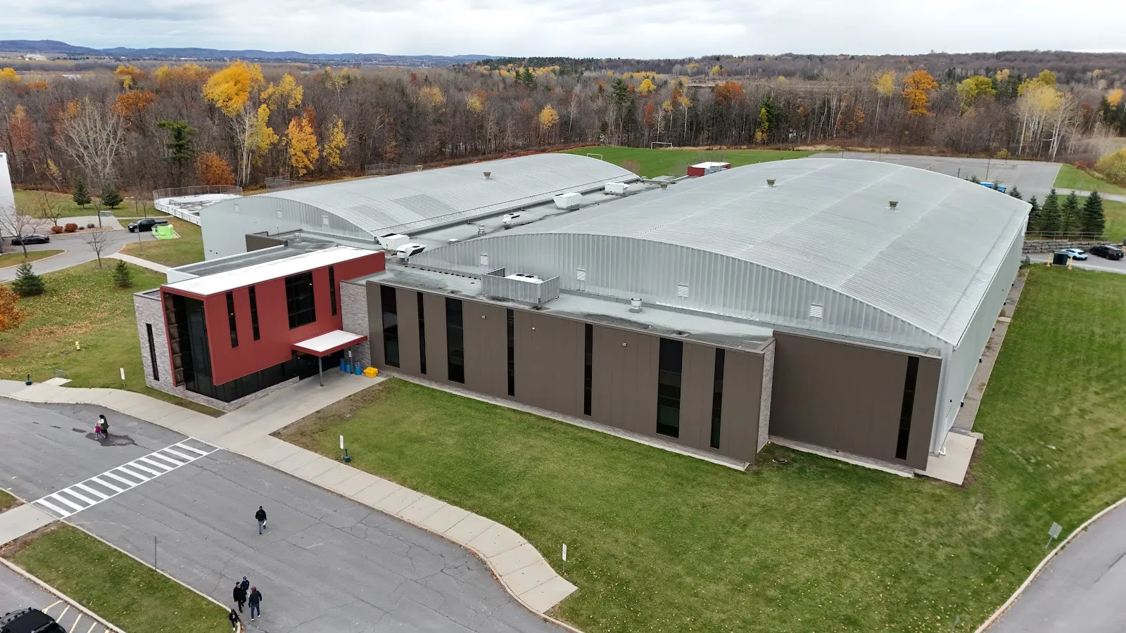 Una vista aérea de la arena de dos pistas, con sus techos curvos de metal y su ala de entrada revestida de rojo, entre áreas de césped. — Desjardins Centre (Rockland)