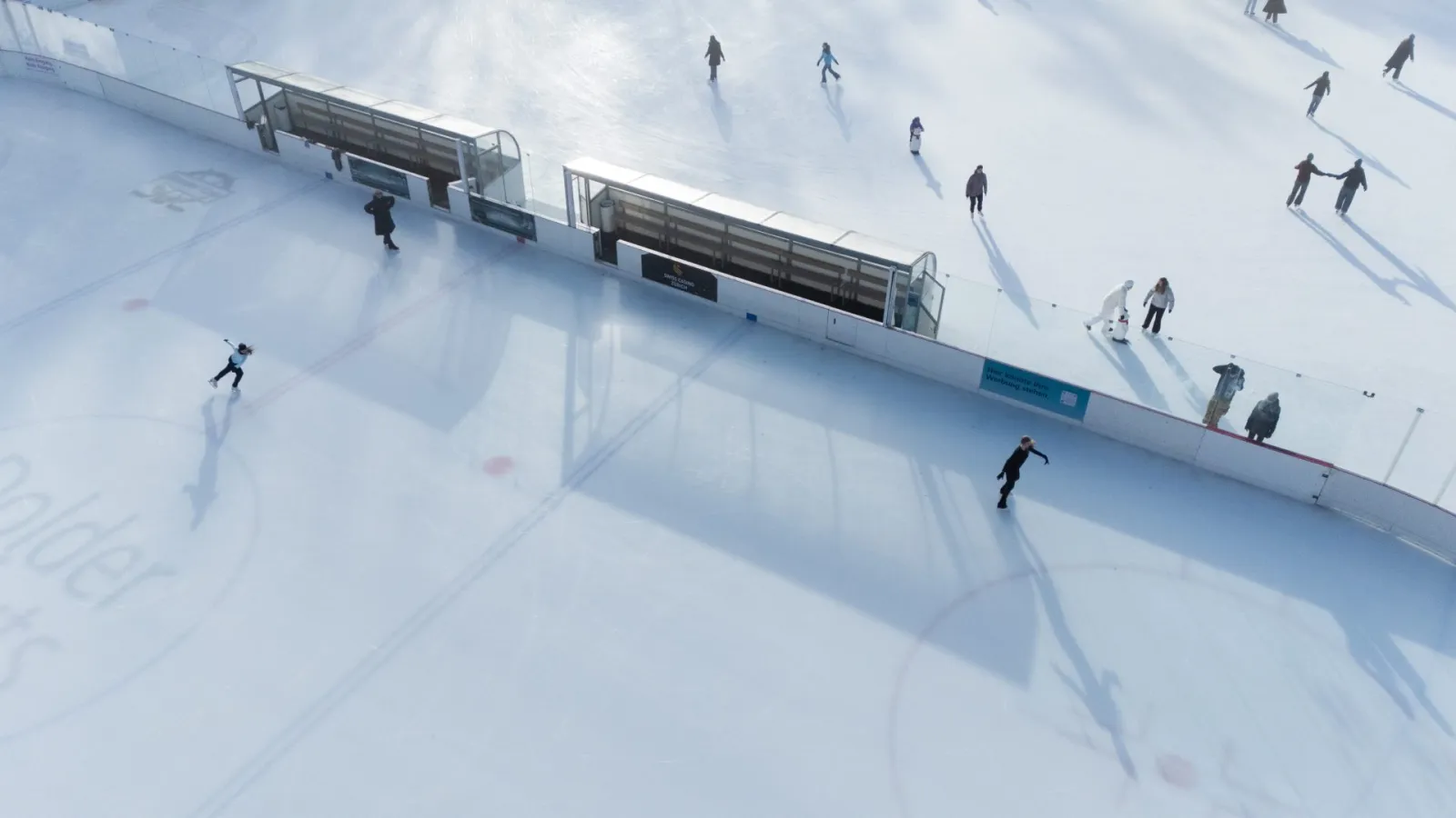 Skaters on the ice of the Dolder Eisbahn, seen from above along the boards and the players' benches — Dolder Eisbahn