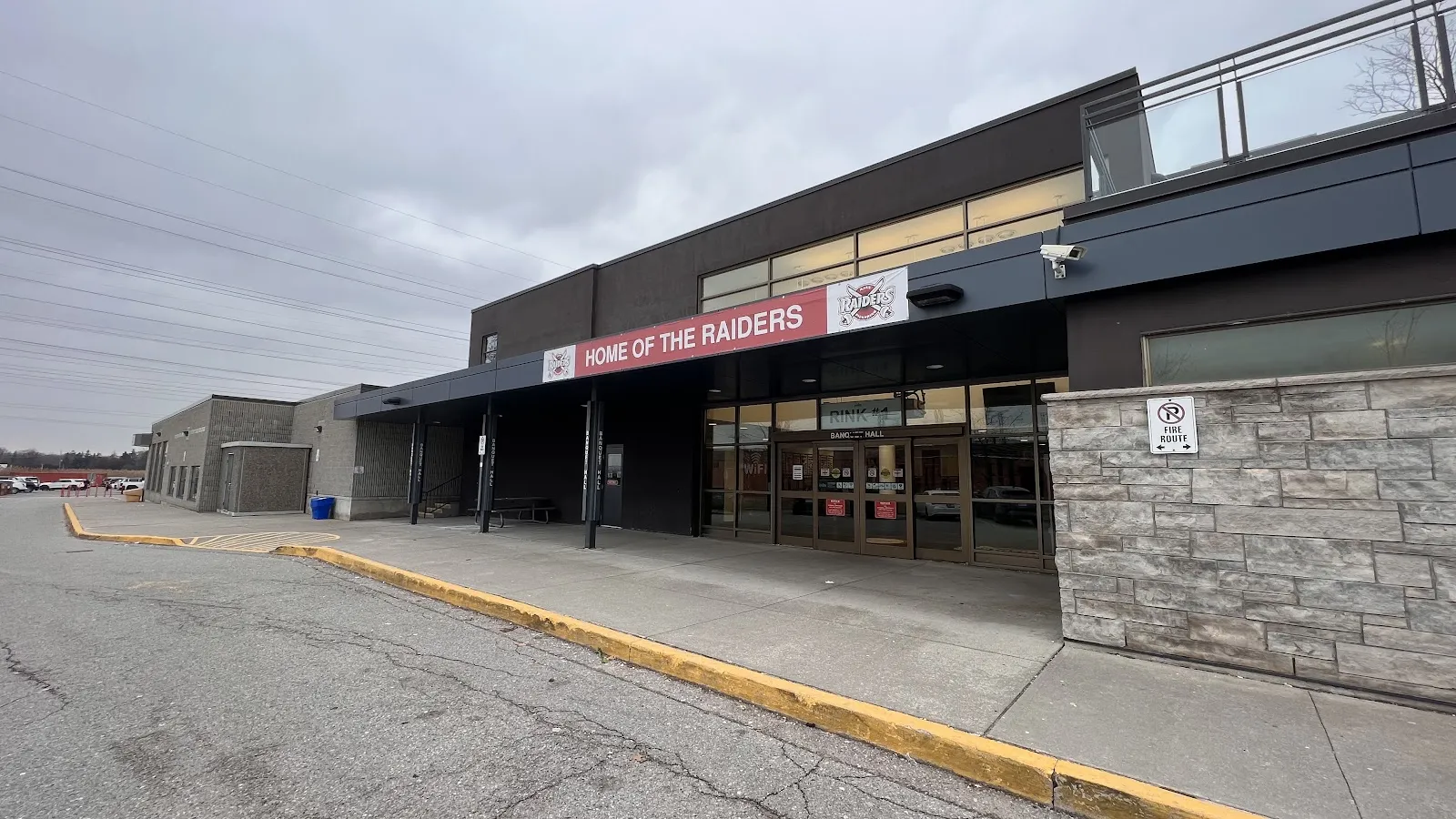 La entrada de Don Beer Arena bajo una manta de Home of the Raiders, con las letras Rink 1 sobre las puertas de vidrio y el salón de banquetes al lado. — Don Beer Arena (Pickering)
