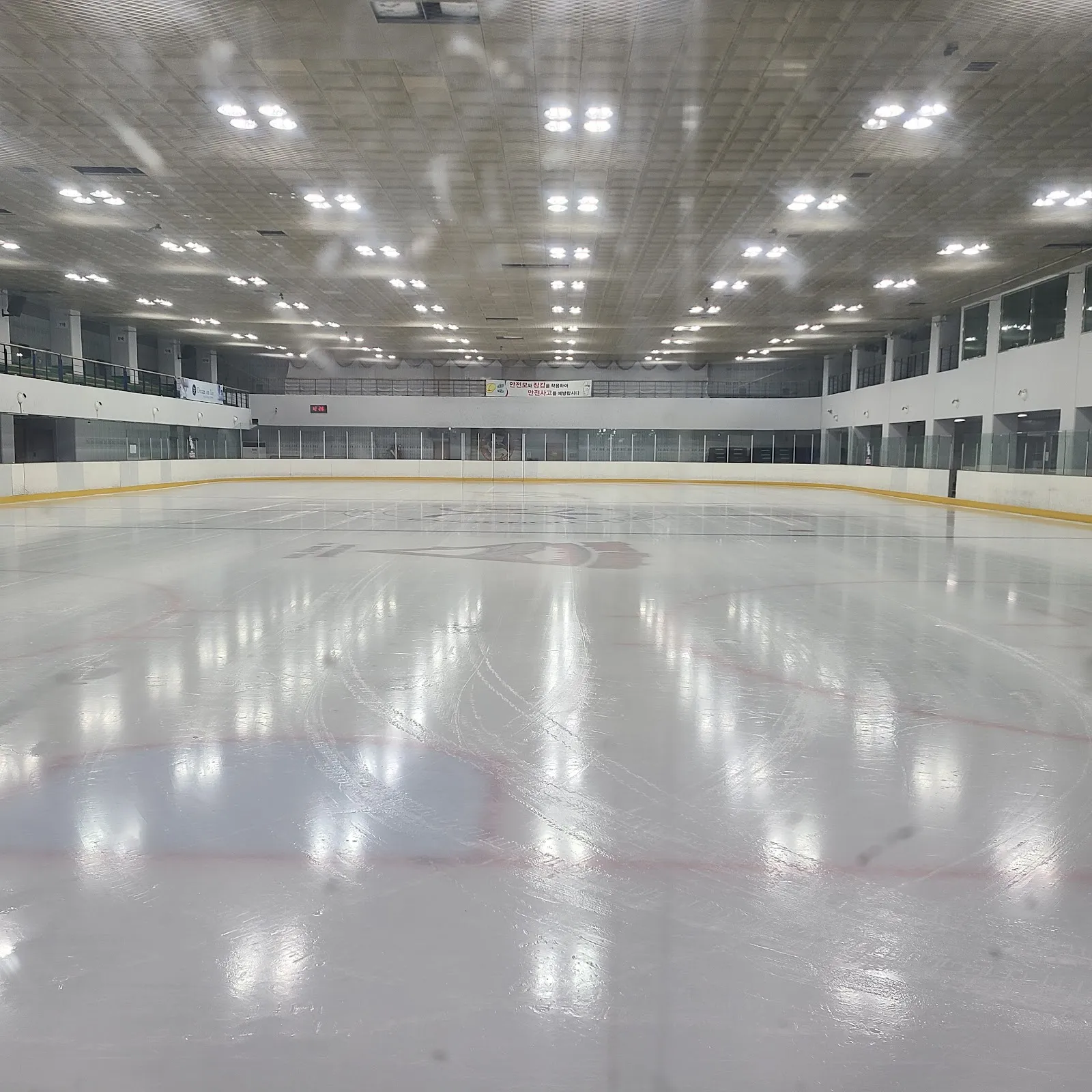 동천 아이스링크 안의 빈 빙판. 노란색 상단의 펜스와 그 뒤의 관람석이 보여요. — Dongcheon Ice Rink