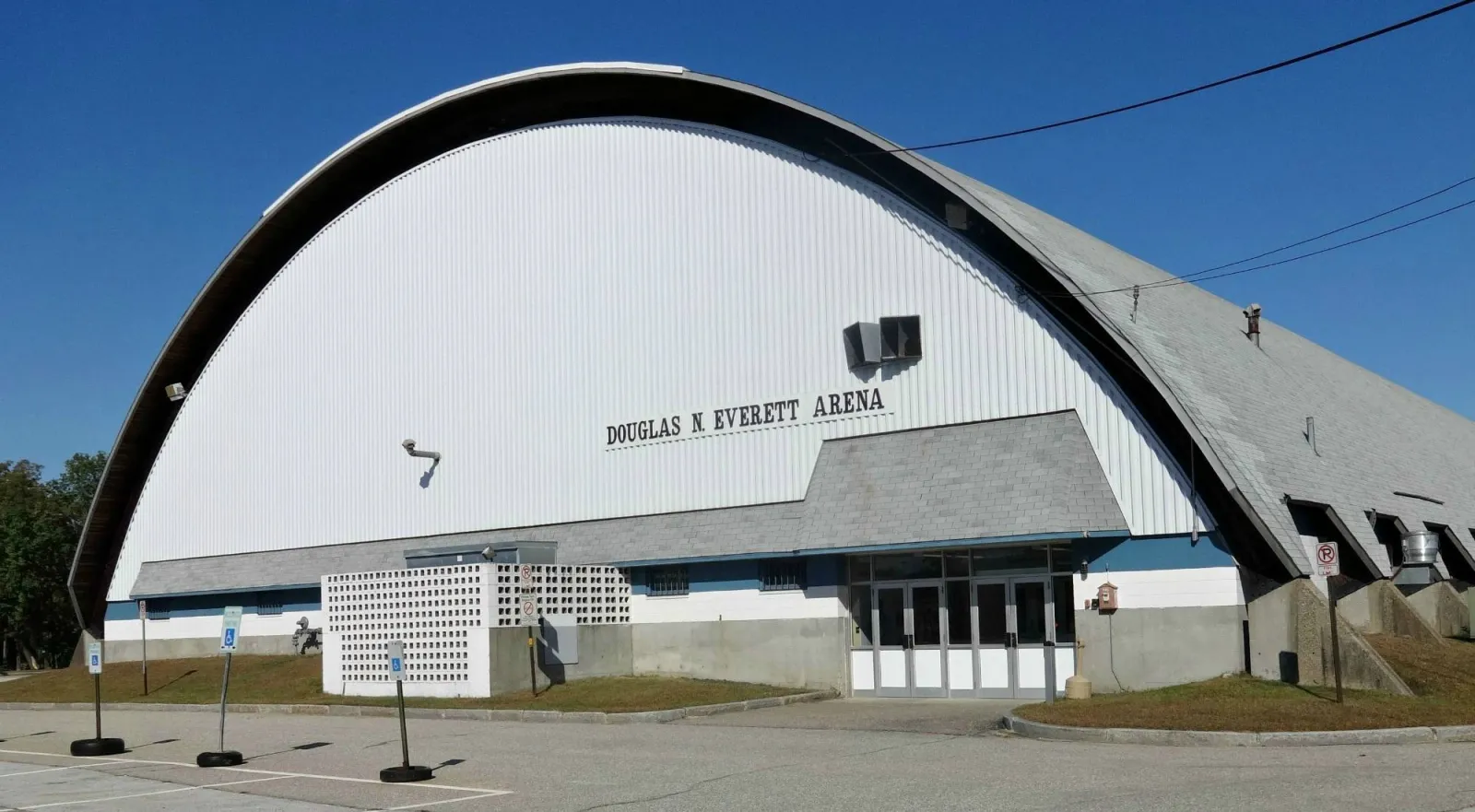 El edificio de la arena estilo nave Quonset desde el estacionamiento, con "DOUGLAS N. EVERETT ARENA" rotulado en el techo curvo de metal blanco sobre la entrada. — Douglas N. Everett Arena