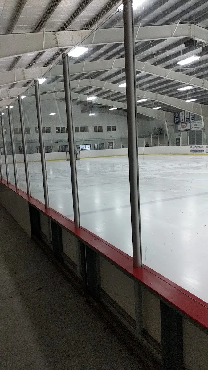 The empty Douro arena ice seen through the glass with the rink boards and a pale roof beyond. — Douro Community Centre