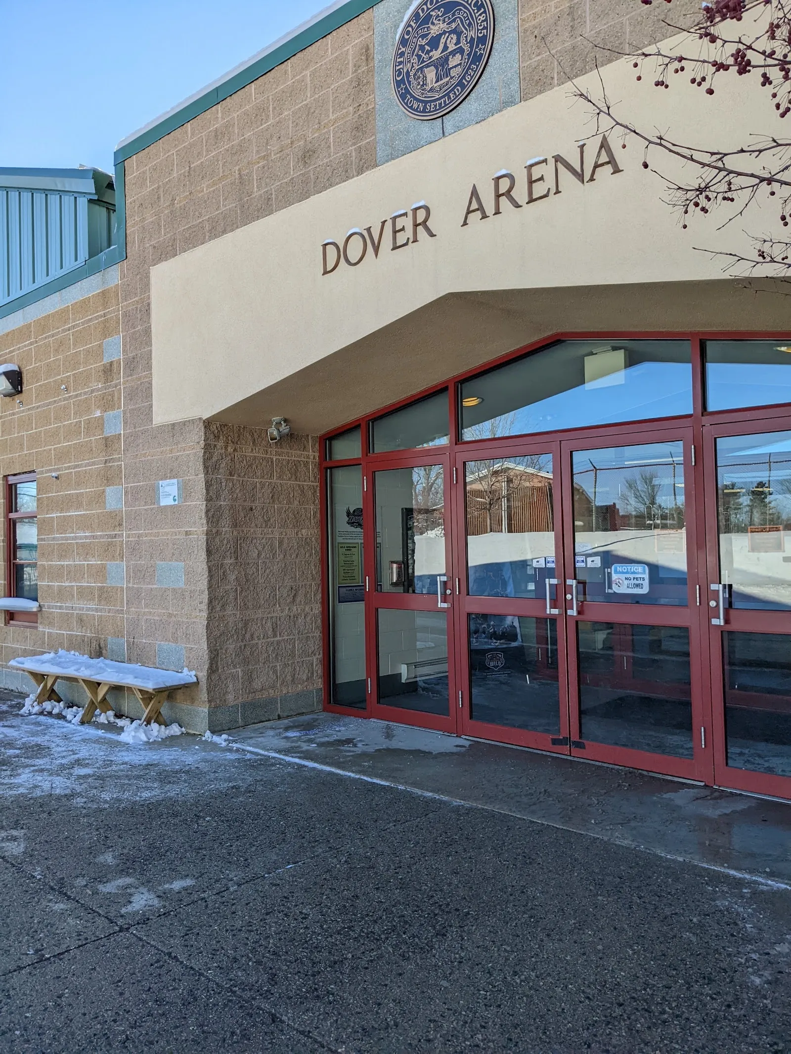 Front entrance of Dover Arena: brick building with "DOVER ARENA" lettering and the City of Dover seal above red-framed glass doors. — Dover Ice Arena