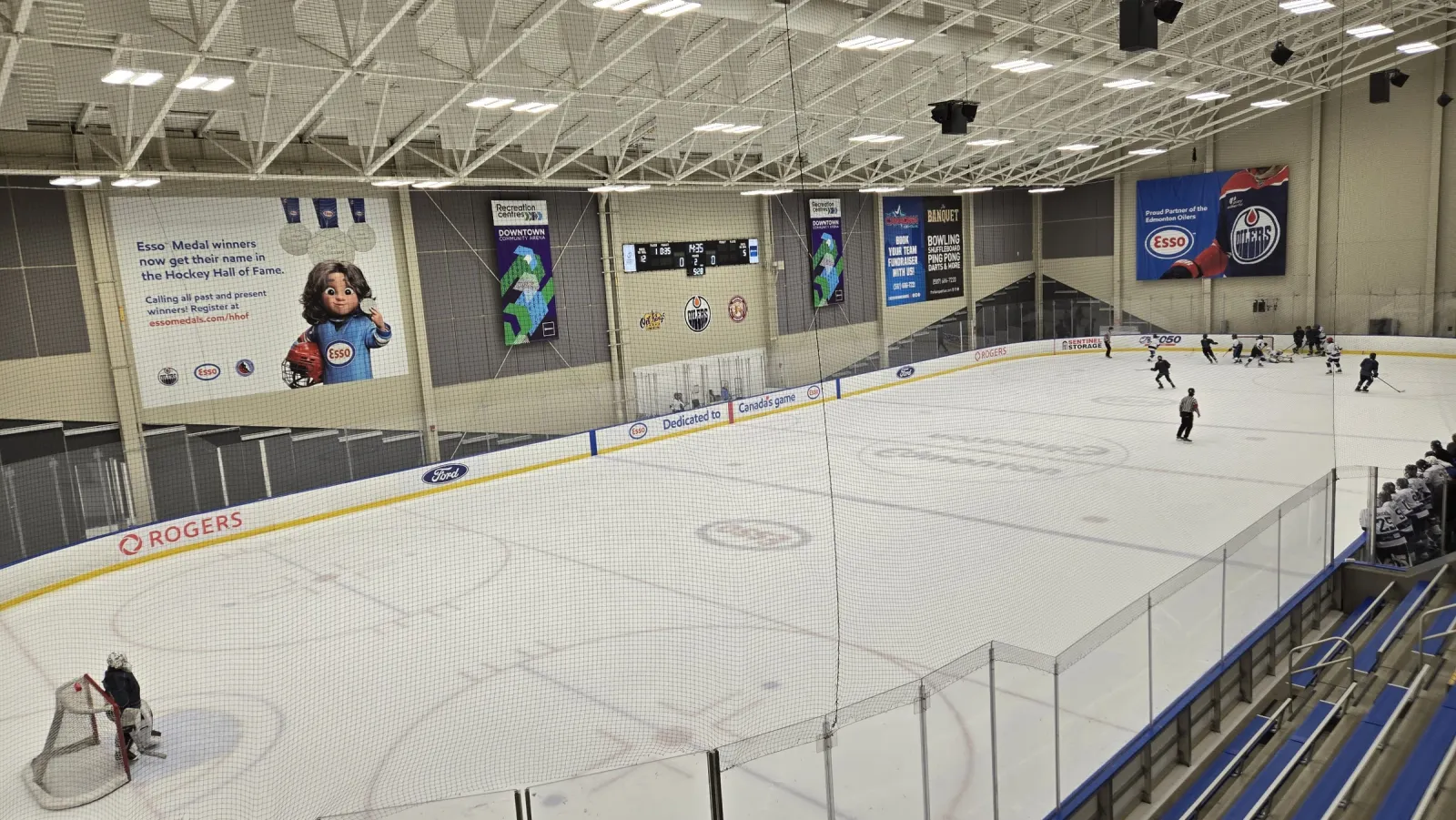 Toda la pista vista desde una esquina de las gradas durante una práctica, con mantas de los Oilers y un mural del Hockey Hall of Fame en la pared del fondo. — Downtown Community Arena