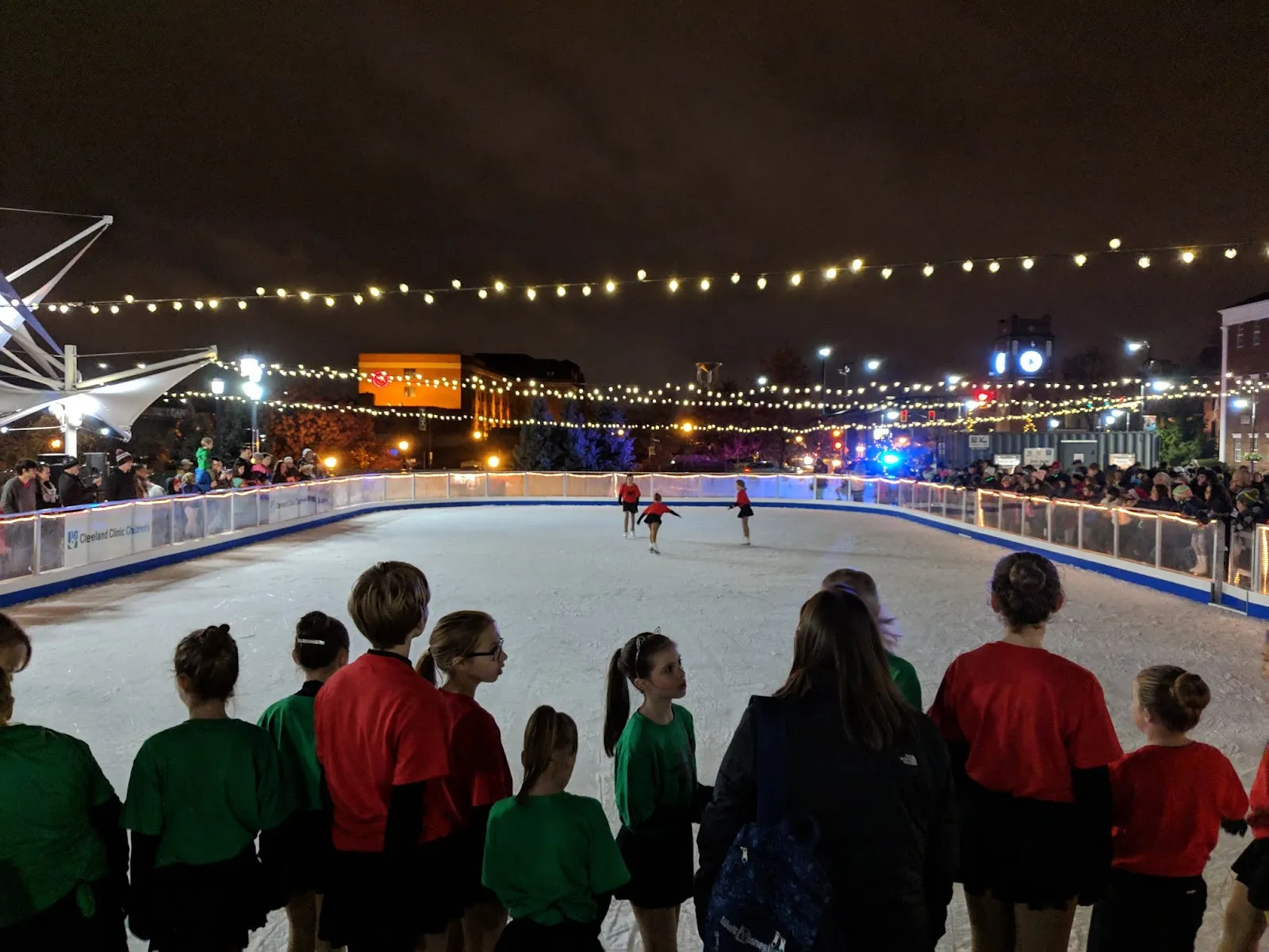 La pista de hielo iluminada del centro de Cuyahoga Falls de noche, con patinadores en el hielo — Downtown Cuyahoga Falls Ice Skating Rink