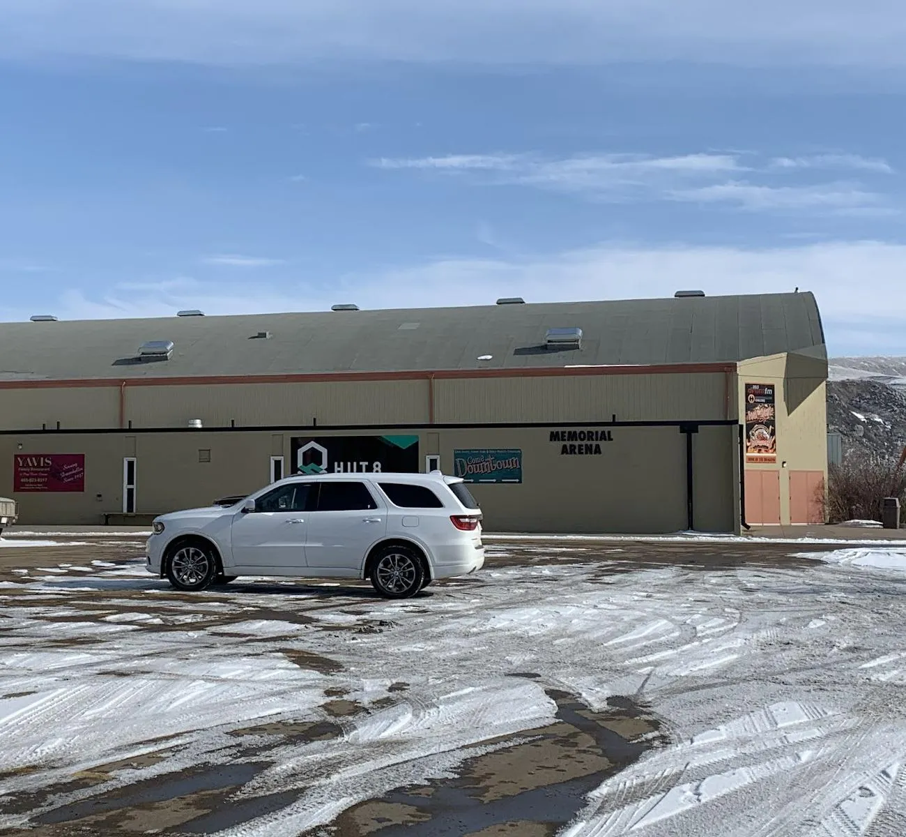 The long, low-roofed Drumheller Memorial Arena, lettered Memorial Arena over its side entrance, across a snowy parking lot. — Drumheller Memorial Arena