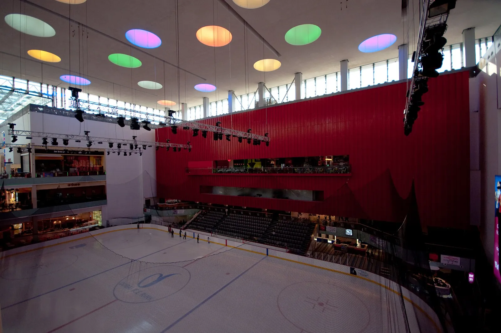 The Olympic-size ice sheet of the Dubai Ice Rink seen from above, with the red wall and stands of the atrium behind it — Dubai Ice Rink