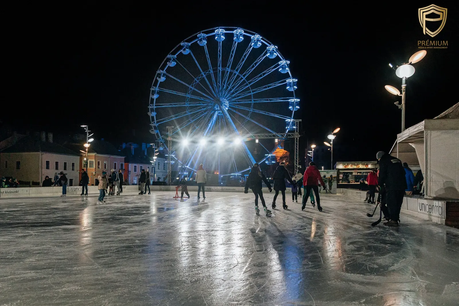 The Dunakapu tér ice rink in Győr at night, with skaters in the distance on the lit ice and a Ferris wheel beside the rink. — Dunakapu téri jégpálya