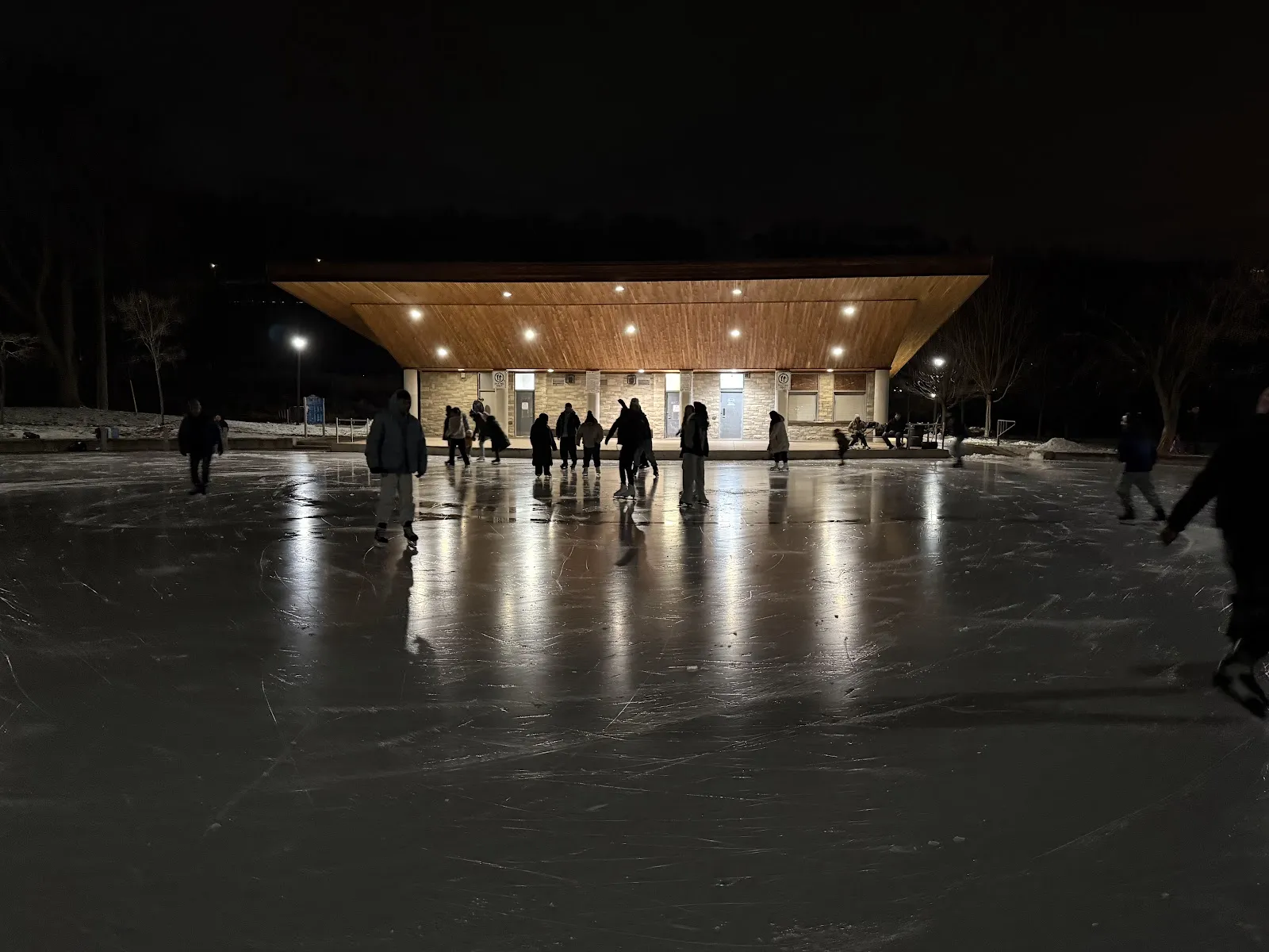 El pabellón del parque del Dundas Driving Park iluminado de noche junto a la pista al aire libre, con patinadores en el hielo a lo lejos — Dundas Driving Park City Outdoor Rink