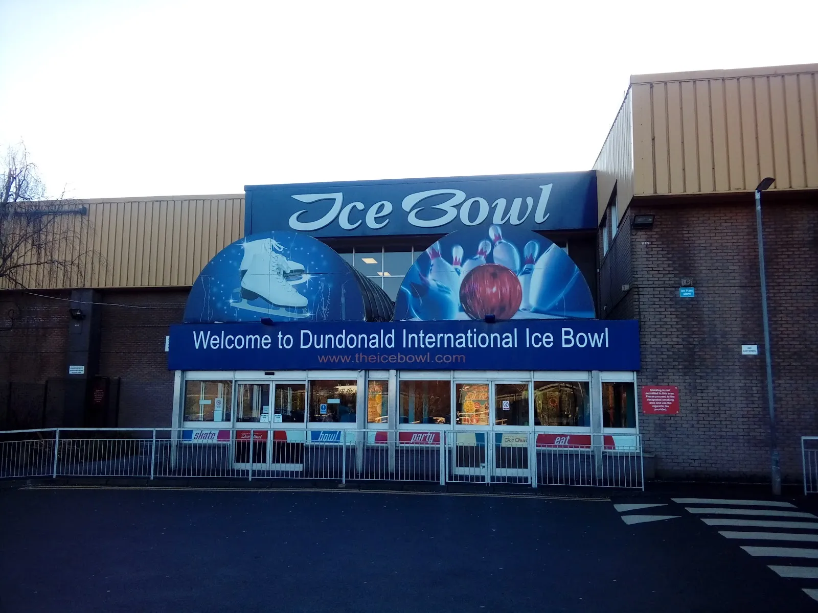 The front of Dundonald International Ice Bowl: the blue 'Ice Bowl' sign with skate and bowling-ball graphics above a 'Welcome to Dundonald International Ice Bowl' banner and the glazed entrance. — Dundonald International Ice Bowl