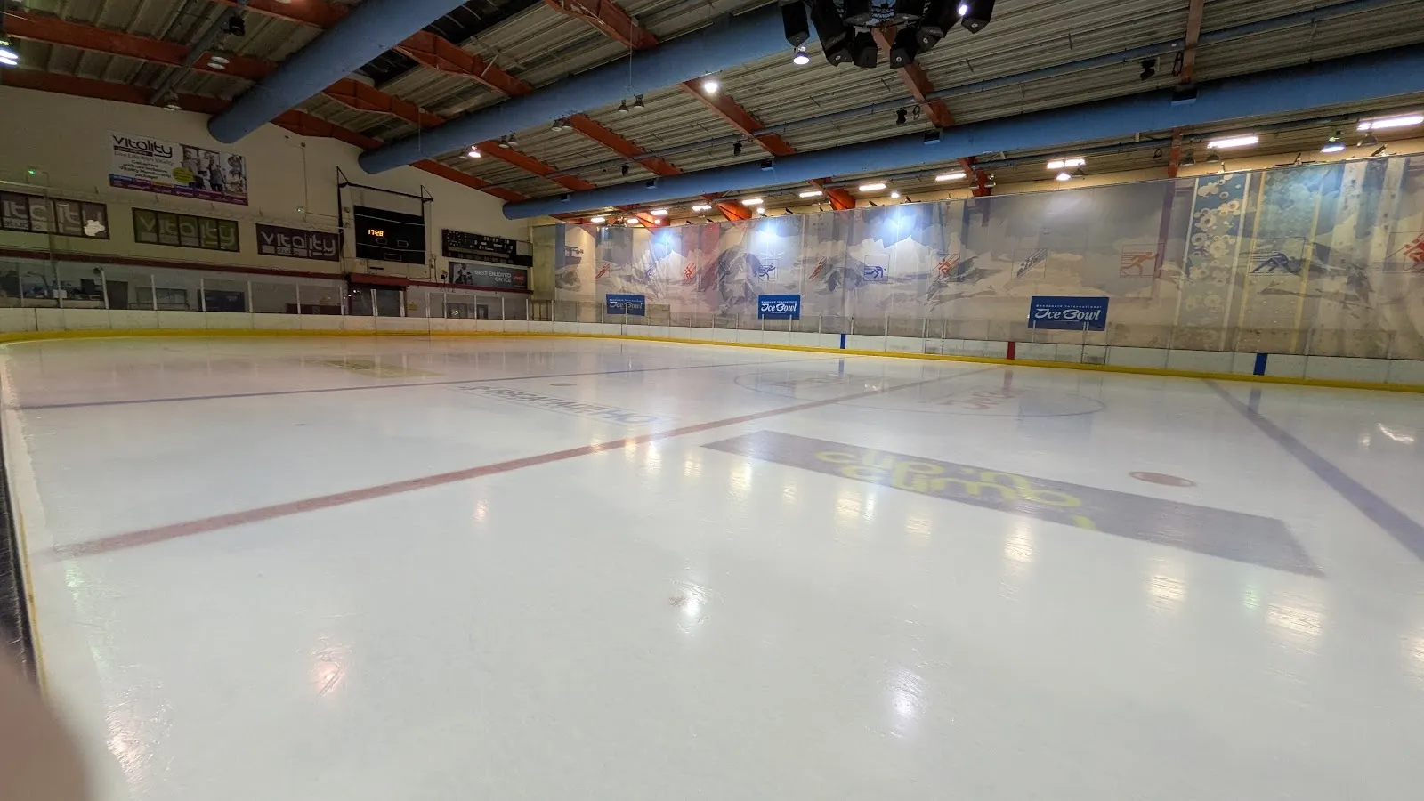 The empty ice sheet of the Dundonald Ice Bowl, with the boards, the painted mountain mural along the far wall and the roof trusses above; no people on the ice. — Dundonald International Ice Bowl
