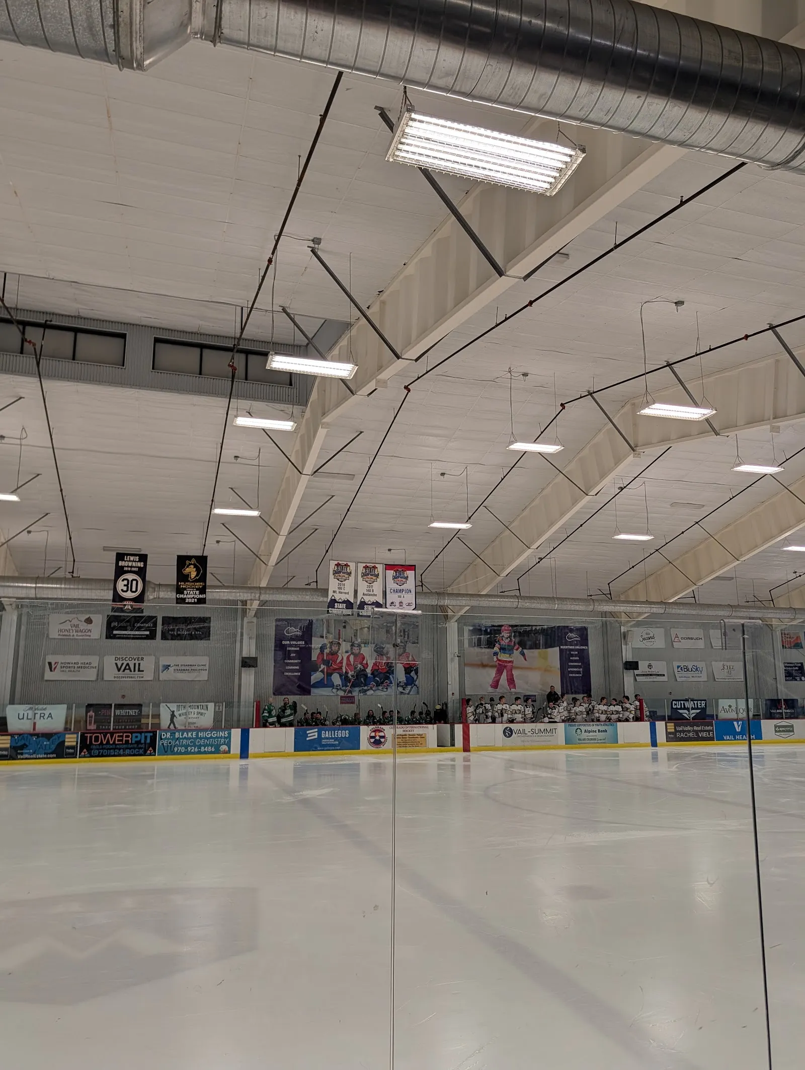 The ice sheet under the arched roof, with team banners and sponsor boards along the far side. — Eagle Pool & Ice Rink