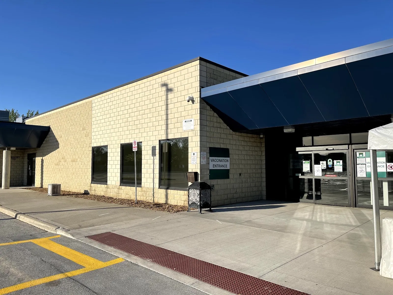 The Earl Nichols Recreation Centre entrance, tan block walls under a dark blue metal canopy with glass doors, on a clear day. — Earl Nichols Arena