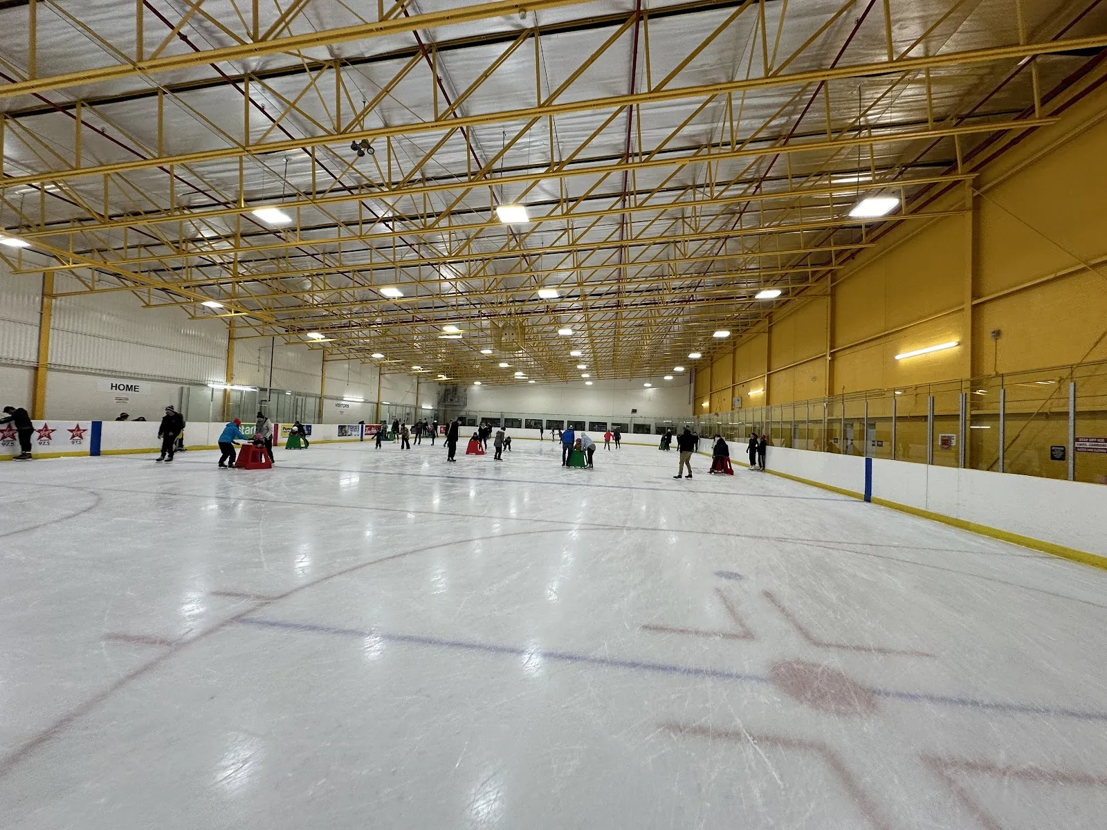 A public skate on one of the Earl Nichols pads, under yellow roof trusses, with skaters spread along the far end. — Earl Nichols Arena