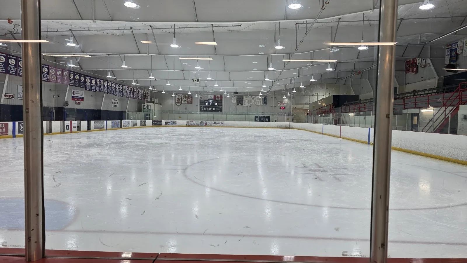 Una pista amplia y vacía vista a través del vidrio, con hielo blanco y tenues círculos bajo un alto techo de acero con un largo techo claro. — East Gwillimbury Sports Complex