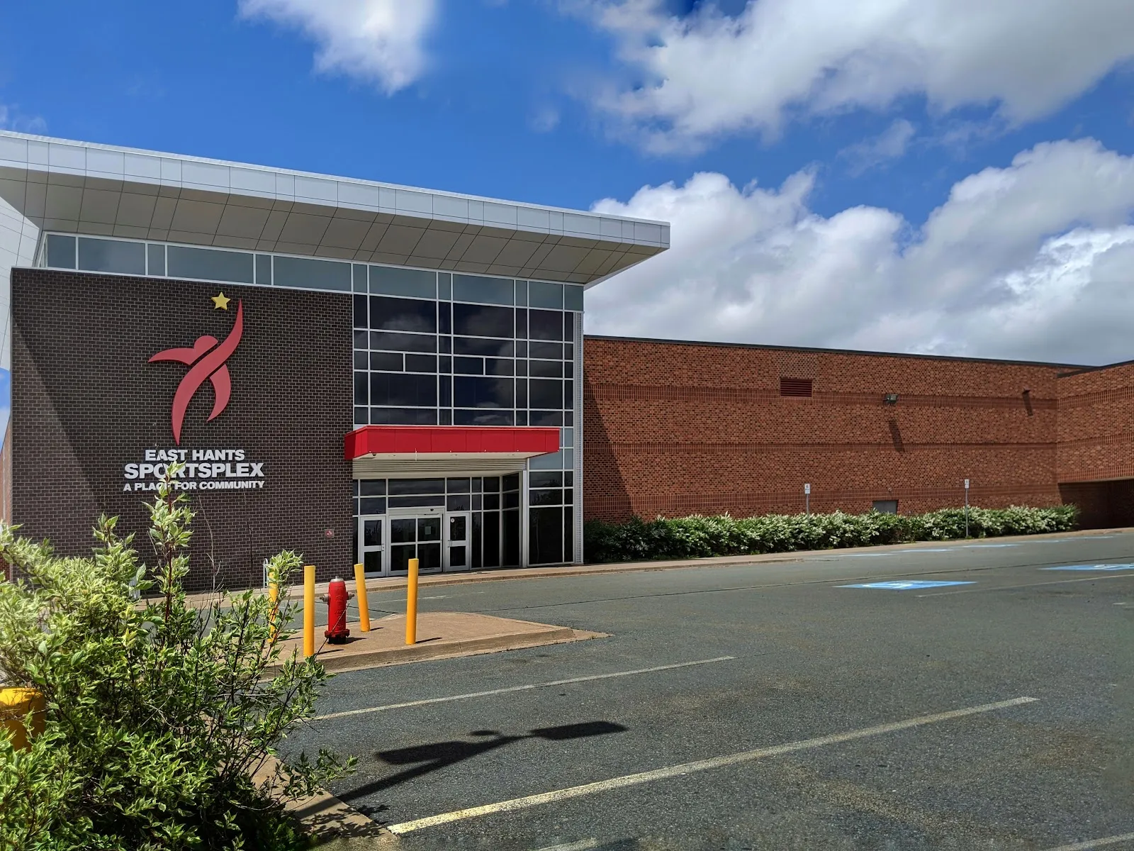 The brick-and-glass front of the East Hants Sportsplex with its star logo sign, seen from the parking lot on a sunny day. — East Hants Sportsplex
