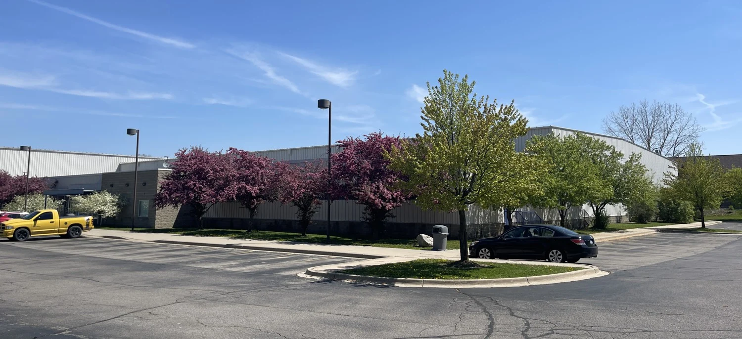 East Lansing Ice Cube's low arena building behind flowering trees and its parking area. — BIGGBY COFFEE Ice Cube - East Lansing