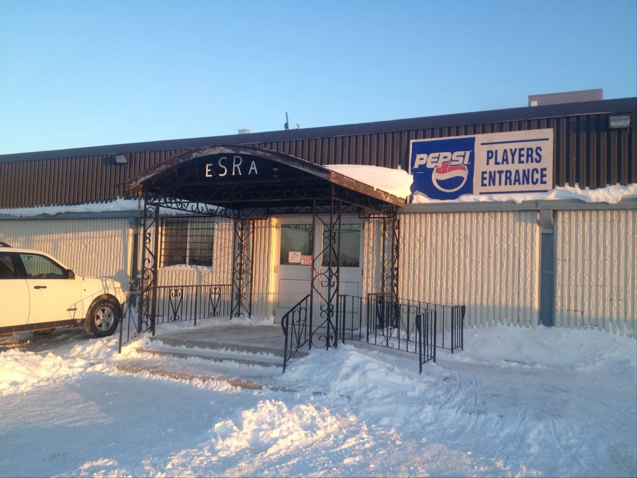The arena's covered side entrance with 'ESRA' over the door and a 'Players Entrance' sign on the metal-clad wall, snow banked in front. — East Selkirk Arena