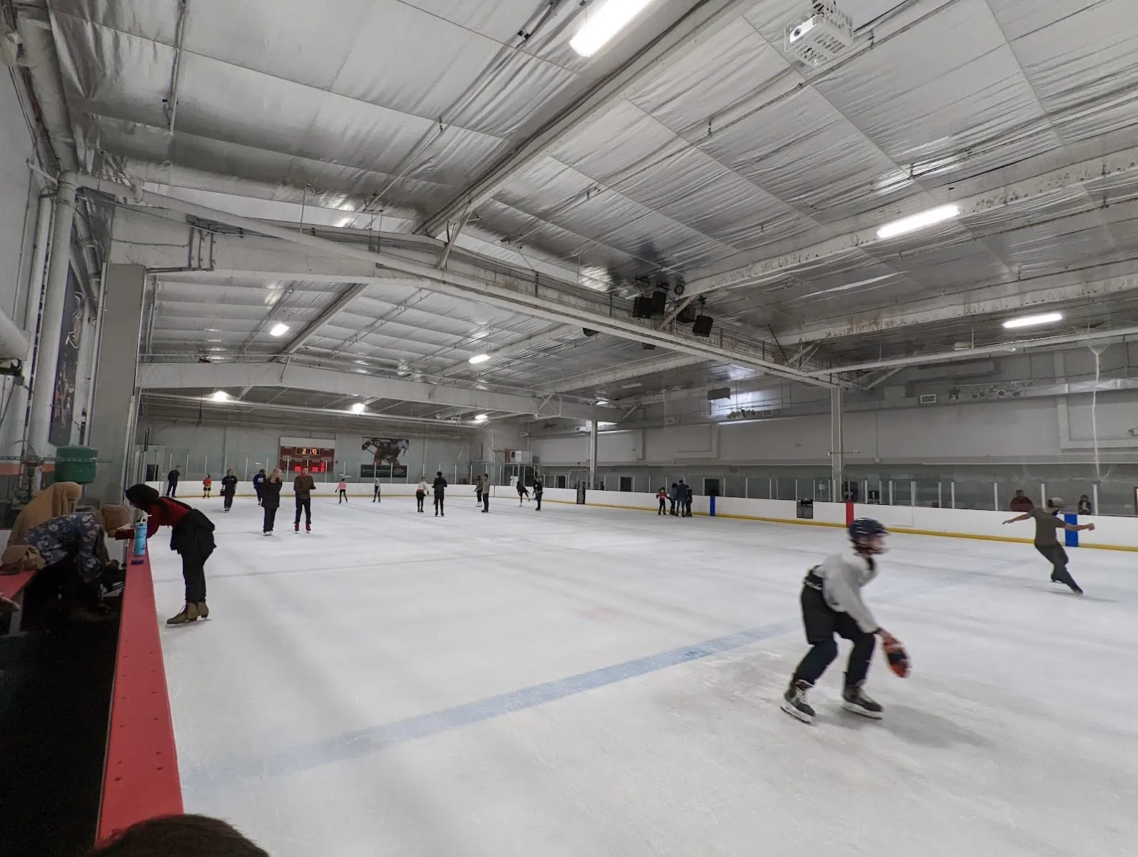 Una vista amplia de la pista de hielo del East West Ice Palace, con patinadores repartidos por el hielo bajo un techo de estructura de acero. — East West Ice Palace