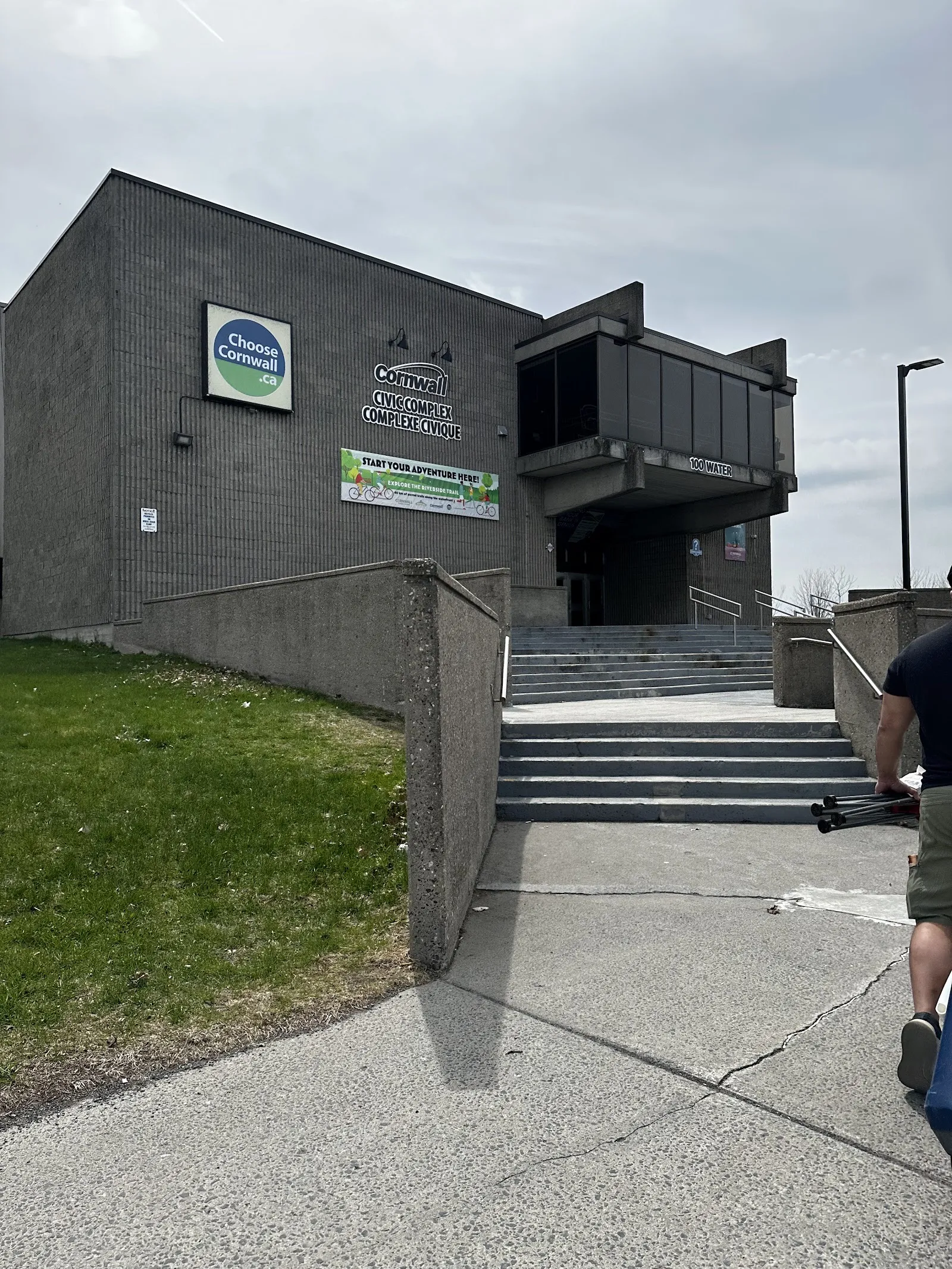 The Cornwall Civic Complex entrance at 100 Water, a grey block building with steps up to a glazed overhang and Civic Complex lettering. — Ed Lumley Arena (Cornwall Civic Complex)