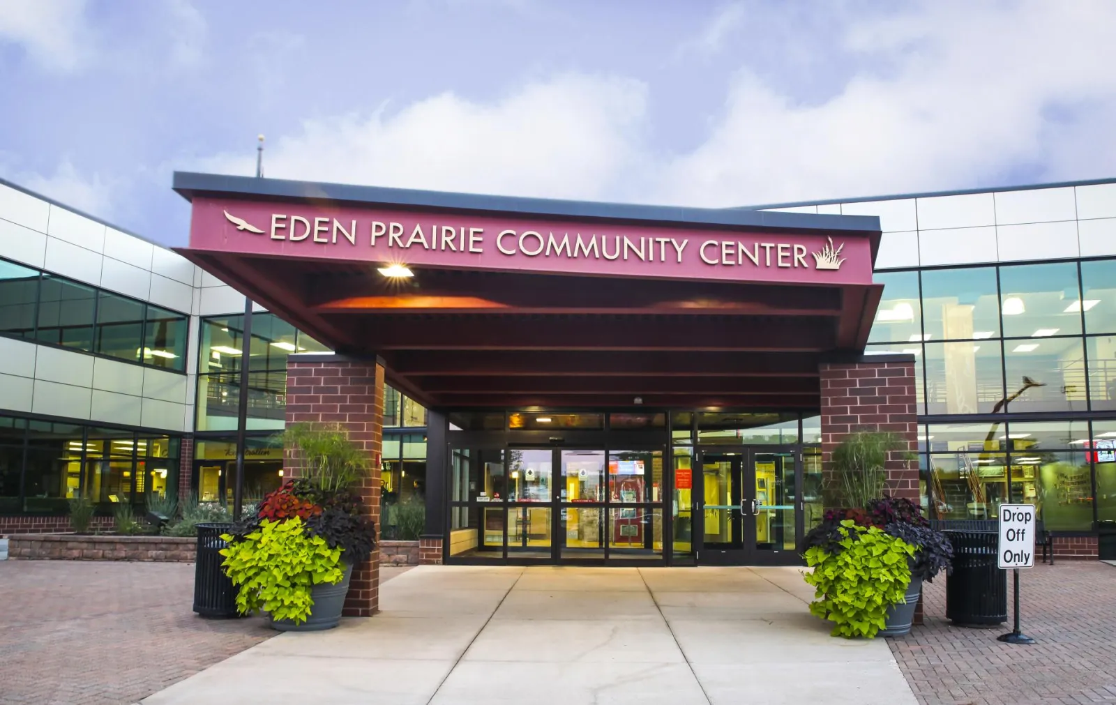 Marquesina de entrada de vidrio y ladrillo que dice EDEN PRAIRIE COMMUNITY CENTER, con el carril para dejar pasajeros y jardineras al frente — Eden Prairie Community Center