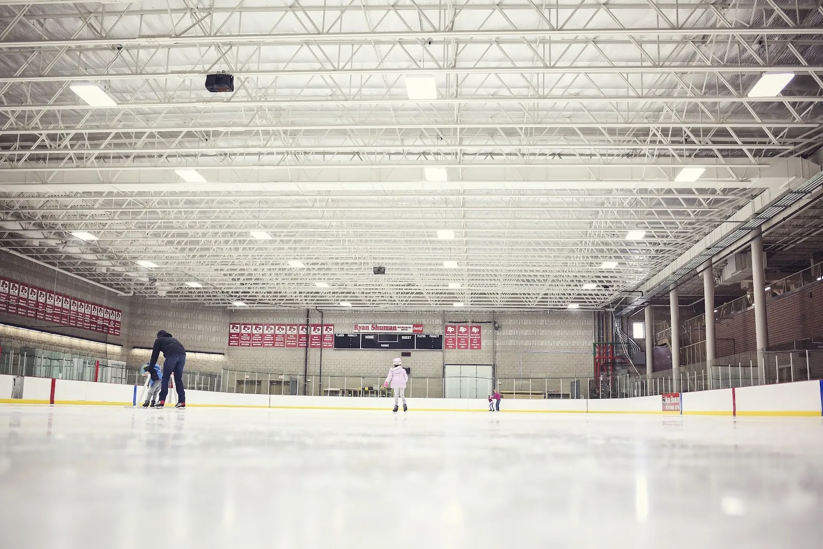 Patinaje público en la Ryan Shuman Memorial Rink a nivel del hielo, bajo armaduras de acero, con las mantas y el marcador de Eden Prairie en el muro del fondo — Eden Prairie Community Center