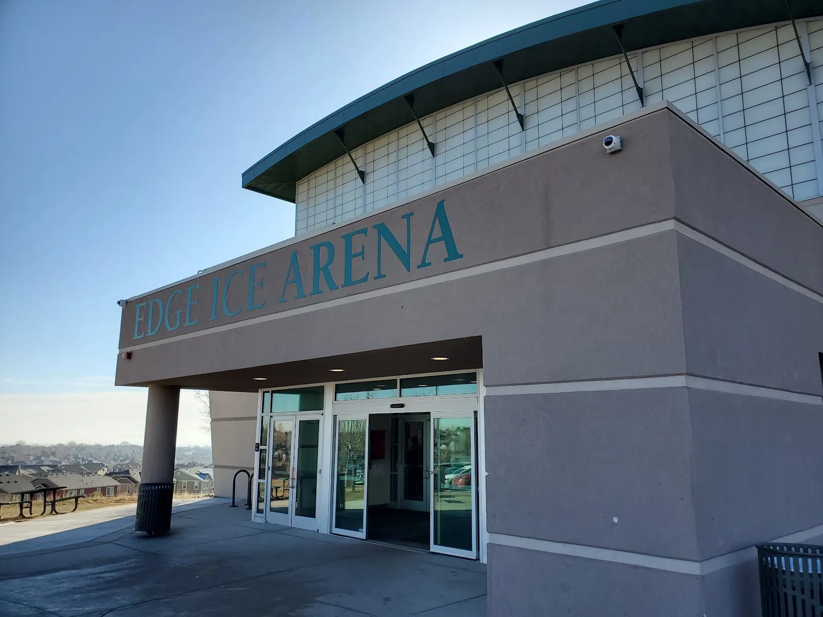 La entrada de Edge Ice Arena: la marquesina de estuco con letras sobre las puertas de vidrio, debajo del techo curvo de la nave de la pista — Edge Ice Arena