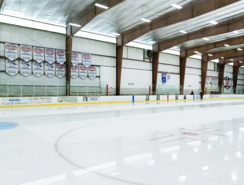 Una pista vacía recién pulida con mantas de campeones estatales colgadas a lo largo de la pared del fondo bajo las armaduras de acero del techo. — The Edge Sports Center