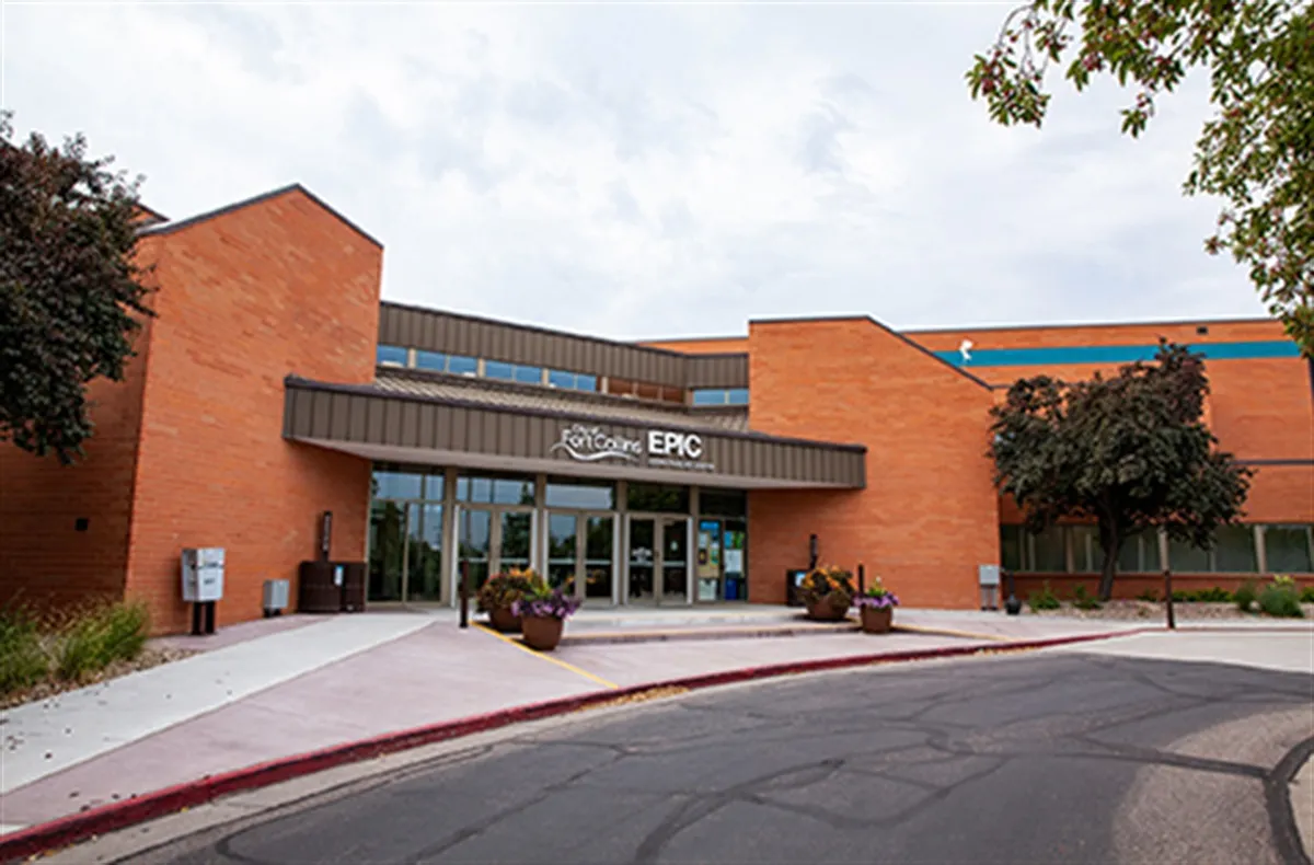 Brick front entrance of Edora Pool Ice Center with a canopy reading "City of Fort Collins EPIC," flower planters, and the striped pool-side clerestory band visible along the roofline. — Edora Pool Ice Center