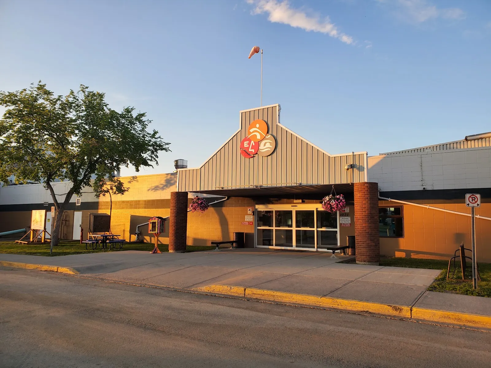 The main entrance of the Edson & District Leisure Centre under its peaked roof and round logo, in low evening sun. — Edson & District Leisure Centre