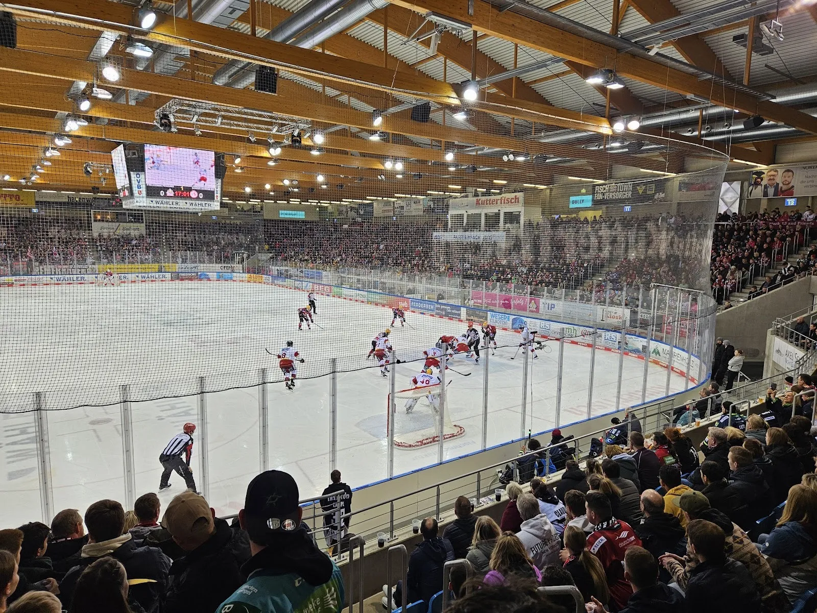 A packed Eisarena Bremerhaven during a hockey match, players across the ice and spectators in the stands under the timber-and-steel roof. — Eisarena Bremerhaven