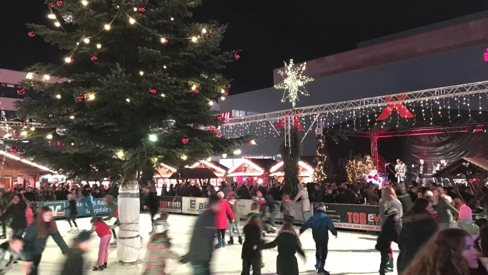 The Eisarena at the Homburger Weihnachtsdorf in the evening, with skaters on the ice around a tall lit Christmas tree. — Eisarena Homburger Weihnachtsdorf