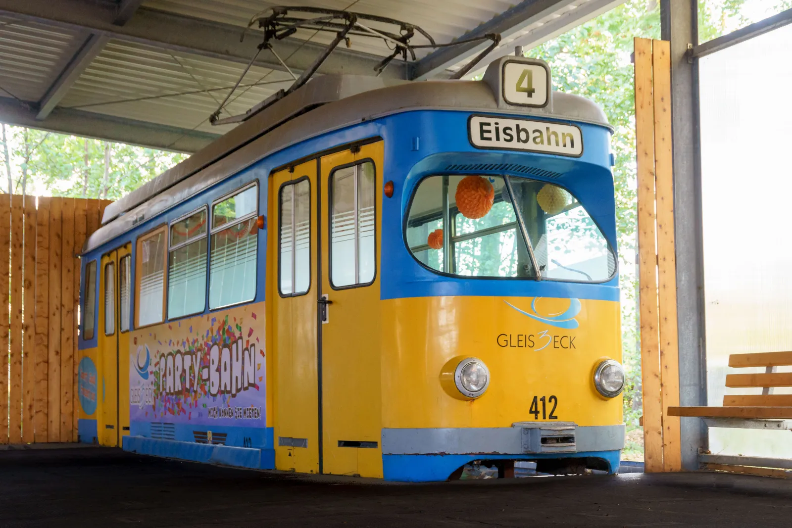 Der gelb-blaue Straßenbahnwagen mit der Aufschrift Eisbahn, der als Vereinsheim der Eisbahn im Freizeitzentrum Gleis3Eck in Waltershausen dient und unter einem Schutzdach steht – Eisbahn im Freizeitzentrum Gleis3Eck Waltershausen