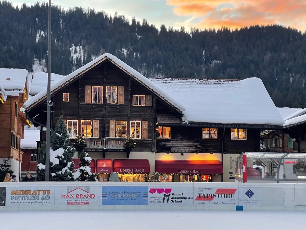 Das Freiluft-Eisfeld mitten in Gstaad, eingerahmt von seinen Werbebanden und den verschneiten Chalets des Dorfs – Eisbahn Gstaad