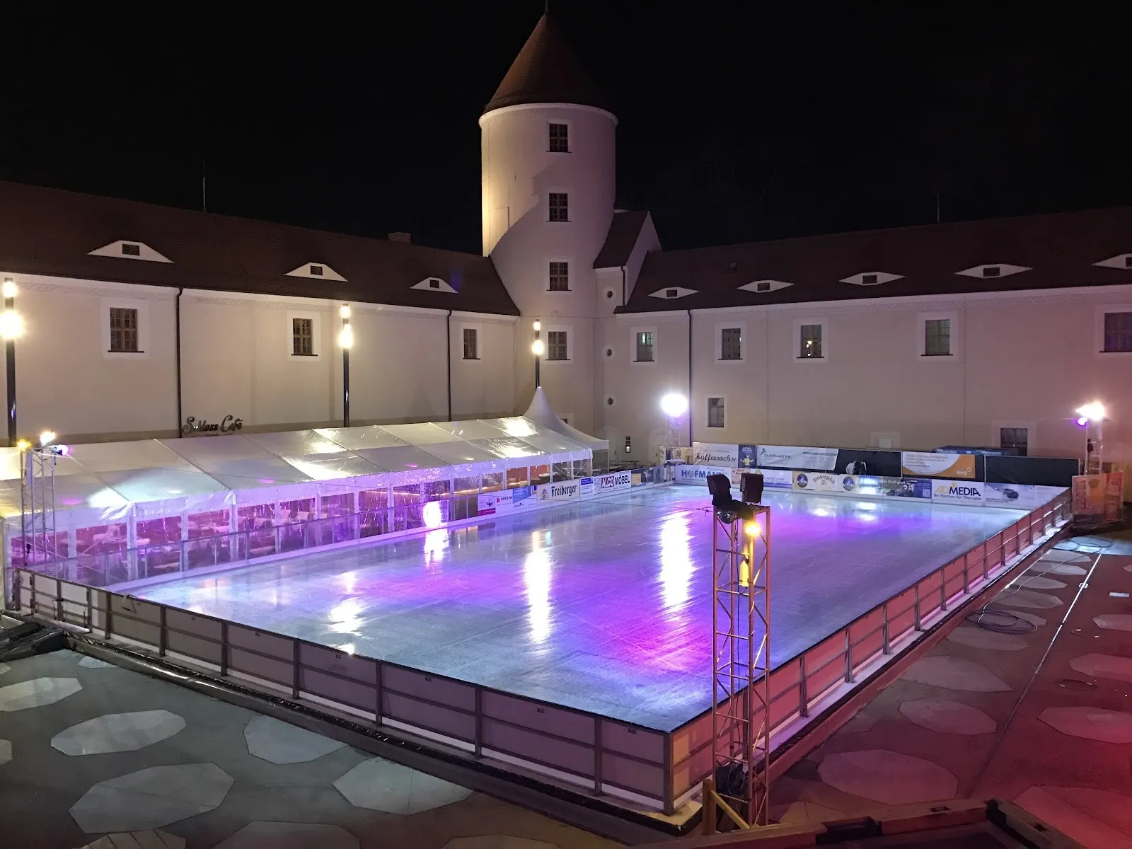 The pop-up ice rink lit in purple in the courtyard of Schloss Freudenstein in Freiberg at night, the castle walls and tower rising around it. — Eisbahn im Schloss Freudenstein