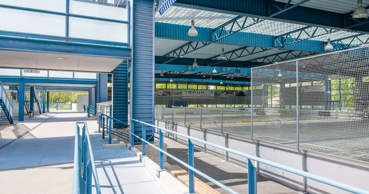 The ice surface of the Eishalle at the Badezentrum Traun seen from the entrance walkway, with boards and glass panels along the rink. — Eishalle im Badezentrum Traun